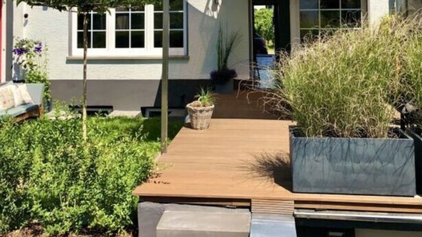 Ein zweistöckiges Haus mit einem Balkon, einer Holzterrasse und einem Garten.
