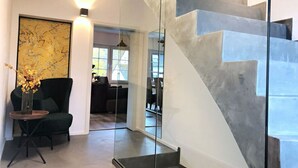 Ein modernes Interieur mit einer Glasstufenwendeltreppe, einem schwarzen Sessel und einer Vase mit Blumen.