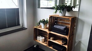 Ein Badezimmer mit einer Holzkonsolen, auf der Handtücher, ein Topf mit einer Pflanze und Toilettenpapier liegen.