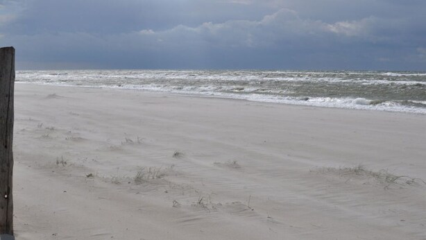 Een zandstrand met golven en een bewolkte lucht.