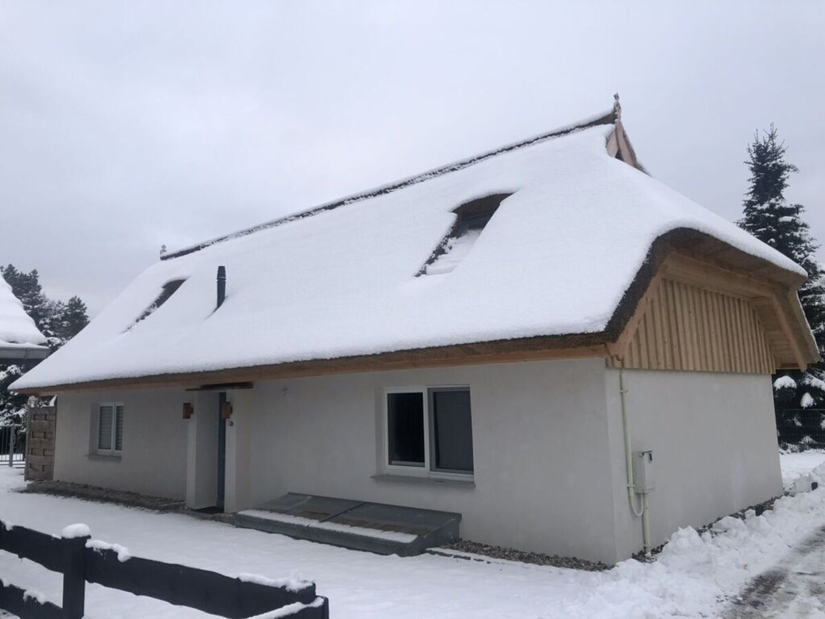 En liten, envåningsbyggnad med ett sluttande tak täckt av snö, en trädörr och en liten veranda.