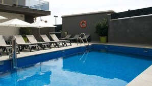 Une piscine avec des chaises longues et des parasols, une bouée de sauvetage accrochée au mur et une plante en pot.