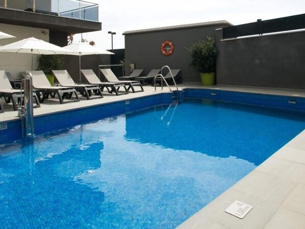 A swimming pool with lounge chairs and umbrellas, a lifebuoy on the wall, and a potted plant. - Belvilla by OYO Apartamento 1 Dormitorio (Fuengirola)