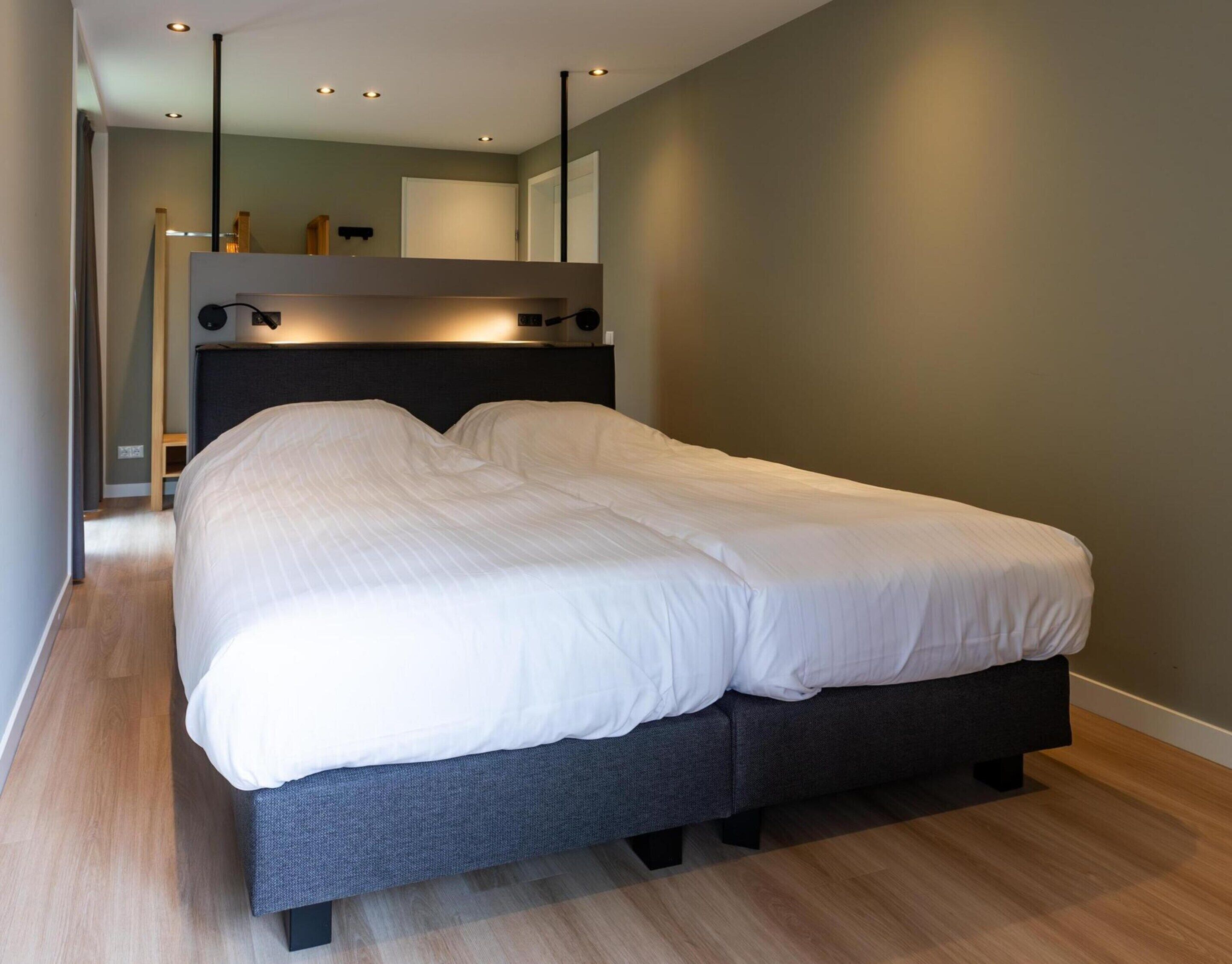 Een moderne slaapkamer met een groot bed, een donker hoofdbord en inbouwspots.