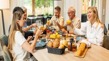 A group of people sitting around a table with breakfast items, including bread, fruits, and drinks.