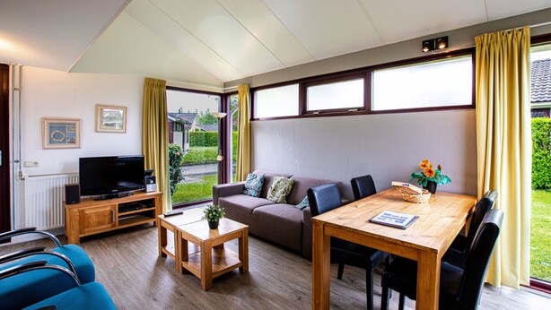 Een ruime woonkamer met een bank, televisie, houten salontafel en een eettafel met stoelen.
