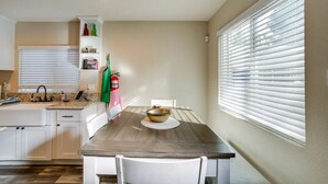 Et kompakt køkken med hvide skabe, en granitbordplade, et spisebord med stole og et vindue med skodder.