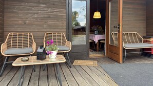 A wooden cabin with a door labeled "Rehfeld" leading to an interior dining area with wicker chairs, a table, and a hanging light fixture. - Blockhaus Mitten in der Natur (Eschede)
