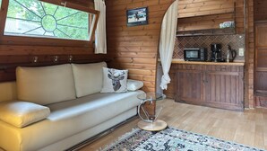 A cozy cabin interior with a sofa, a glass table, a kitchen area with a microwave, and a patterned rug. - Blockhaus Mitten in der Natur (Eschede)