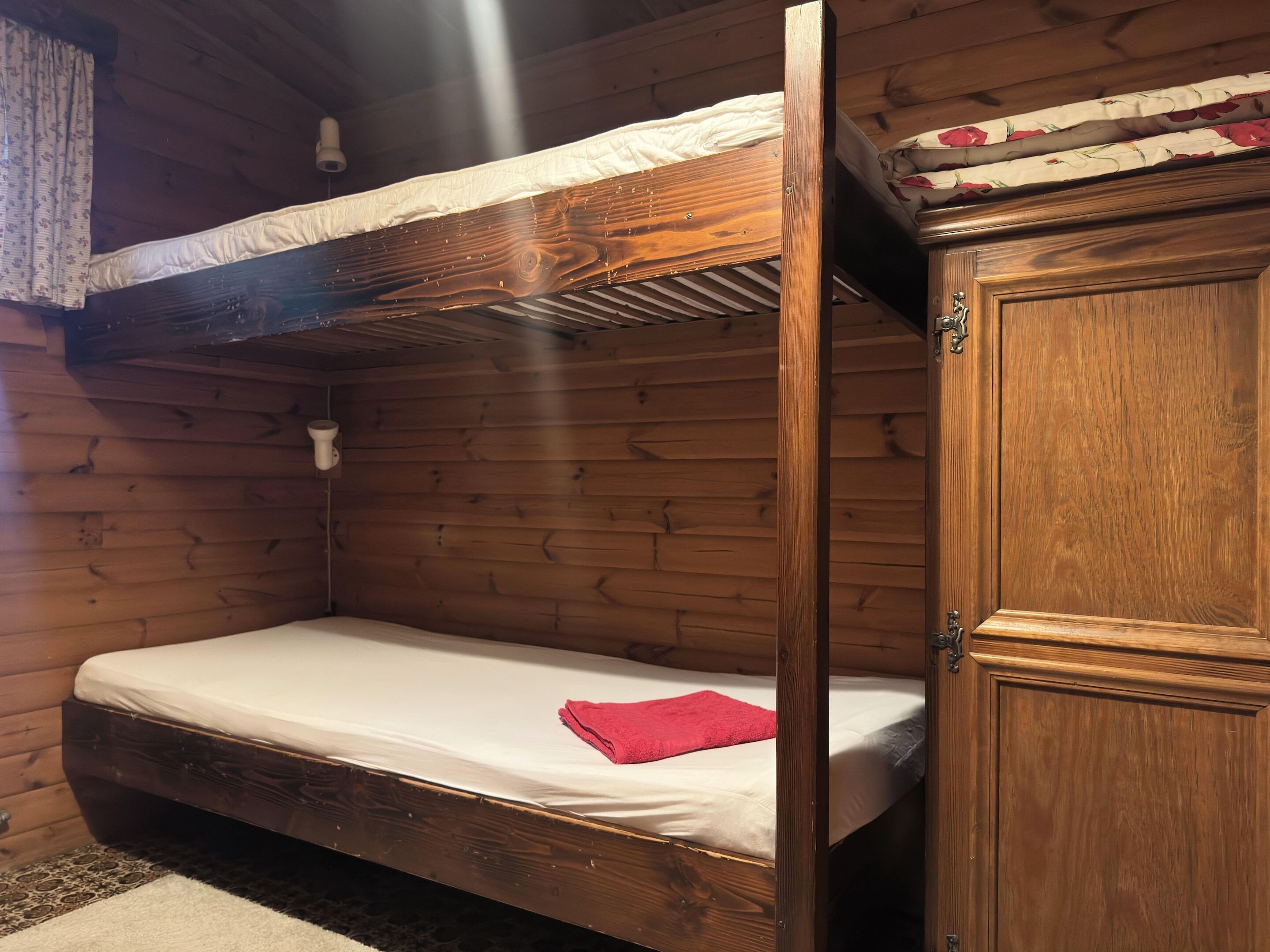 A bunk bed with a red towel on the lower bunk, wooden walls, and a wooden cabinet.
