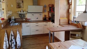 A compact kitchen with white cabinets, a wooden countertop, and a small dining table. - Tonnihuus Comfortable Holiday Residence (Toenning)