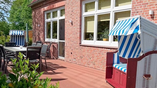 A patio area with a brick wall, a table with chairs, and a striped umbrella. - Tonnihuus Comfortable Holiday Residence (Toenning)