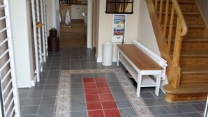 A hallway with a wooden bench, a tiled floor, a staircase, and a kitchen in the background. - Tonnihuus Comfortable Holiday Residence (Toenning)