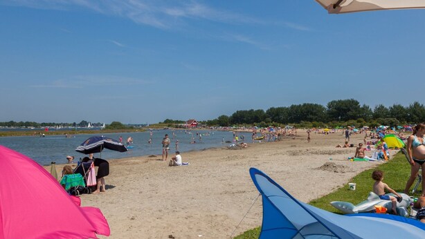 A beach with people relaxing and sunbathing, tents, and a body of water in the background. - Welcoming Family Home (Wolphaartsdijk)