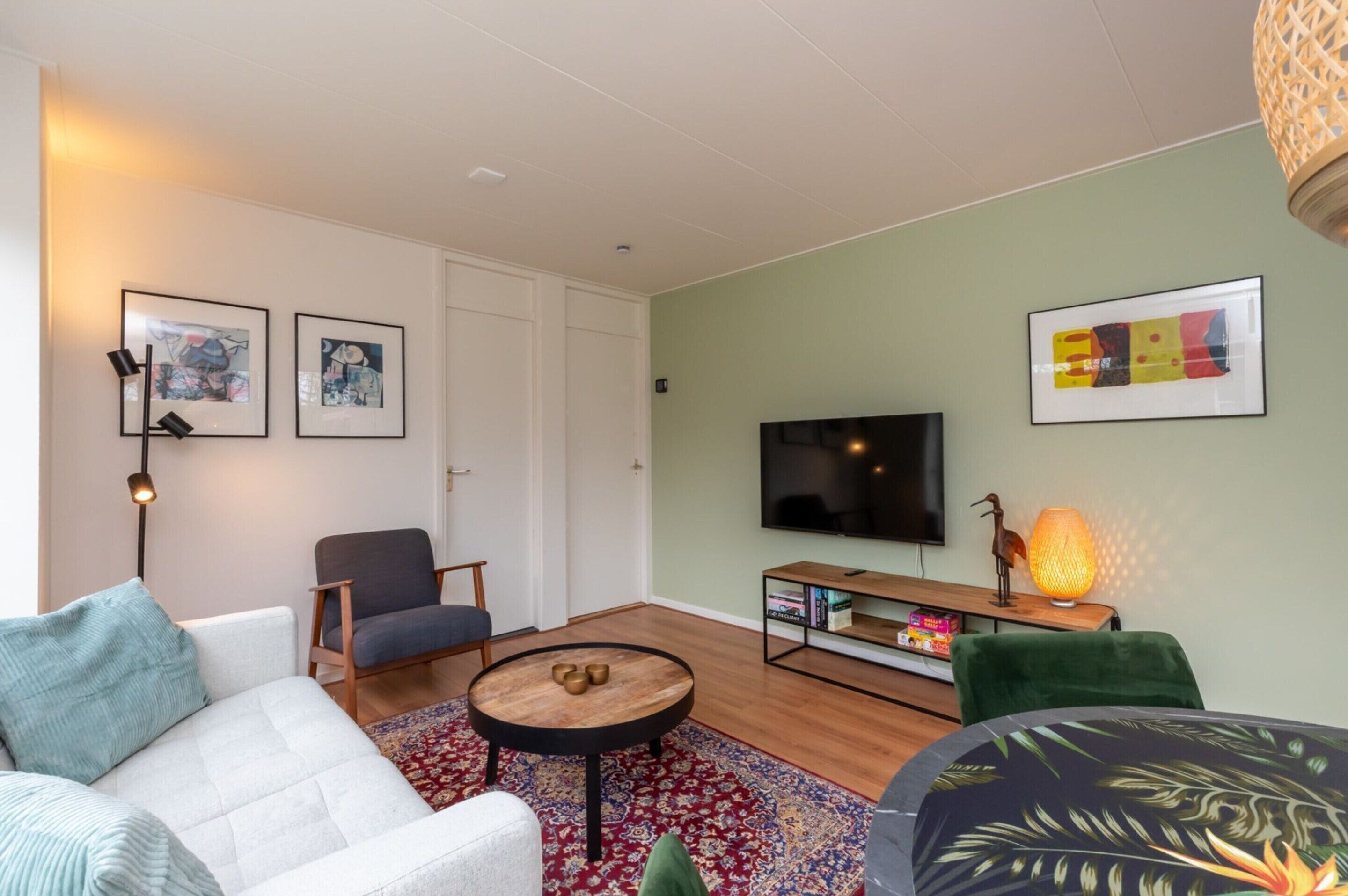 Ein modernes Wohnzimmer mit Sofa, Sessel, rundem Couchtisch und Fernseher.