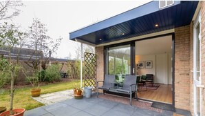 A modern patio with a bench, potted plants, and a view into the house. - Welcoming Family Home (Wolphaartsdijk)
