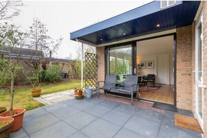 Un patio moderno con un banco, plantas en macetas y vista hacia la casa.
