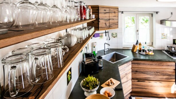 A kitchen with wooden shelves holding glassware, a sink, and various kitchen items. - Fisherman's House Comfortable Holiday Residence (Dießen am Ammersee)