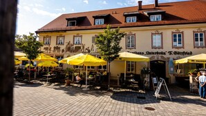 An outdoor seating area with yellow umbrellas, a cobblestone pavement, and a building with a traditional facade and a sign reading "Gasthof Intenbräu F. Götsfried". - Fisherman's House Comfortable Holiday Residence (Dießen am Ammersee)
