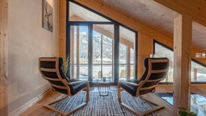 A room with two wooden chairs, a rug, and large windows offering a view of snow-capped mountains. - Spacious Apartment With Sauna (Haus)