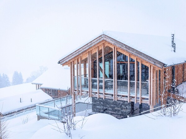 A wooden cabin with large windows and a stone foundation, surrounded by snow. - Spacious Apartment With Sauna (Haus)