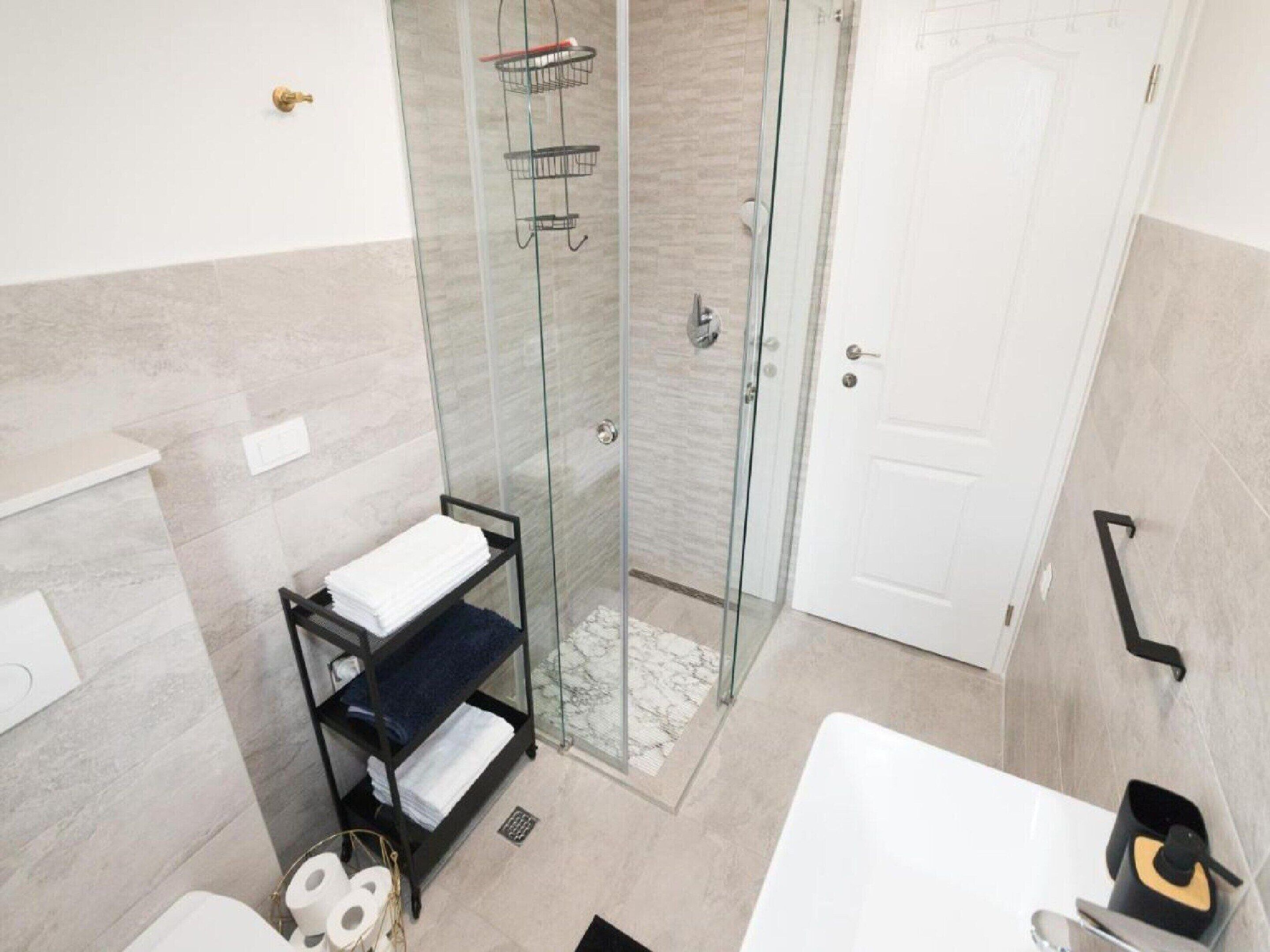 A modern bathroom with a glass shower enclosure, a white sink, and a towel rack.