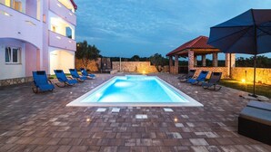 A swimming pool with lounge chairs and a covered seating area, surrounded by a brick patio and a two-story building with balconies. - Apartments Mistral - Three Bedroom Apartment With Balcony and Shared Pool (Razanac)