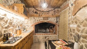A rustic kitchen with a stone wall, wooden beams, a brick oven, and a dining area with a table set for a meal. - Apartments Mistral - Three Bedroom Apartment With Balcony and Shared Pool (Razanac)