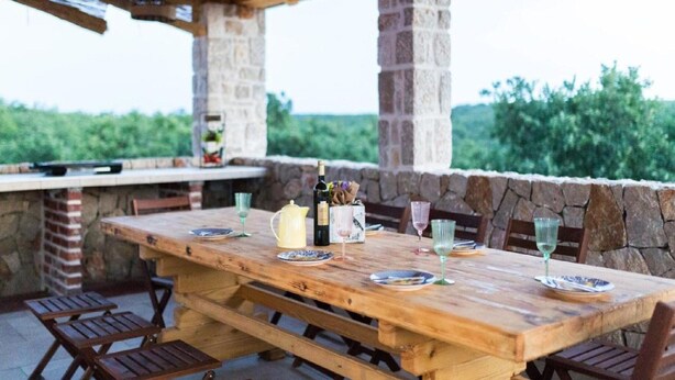 An outdoor wooden table set for dining with stone pillars, surrounded by wooden chairs. - Apartments Mistral - Three Bedroom Apartment With Balcony and Shared Pool (Razanac)