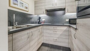 Una cocina moderna con armarios de madera clara, encimera negra, electrodomésticos de acero inoxidable y un cuadro colgado sobre el fregadero.