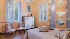 A bedroom with a bed, two chairs, a dresser, and a chandelier. - Apartment Sofia by Interhome (Moneglia)