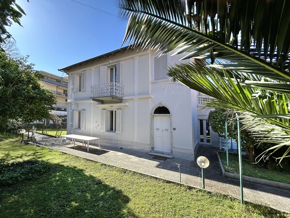 A two-story building with a balcony, a door, and a small table in the front yard.