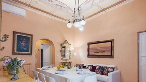 A dining area with a table set for four, white chairs, a white sofa, and a chandelier. - Apartment Sofia by Interhome (Moneglia)