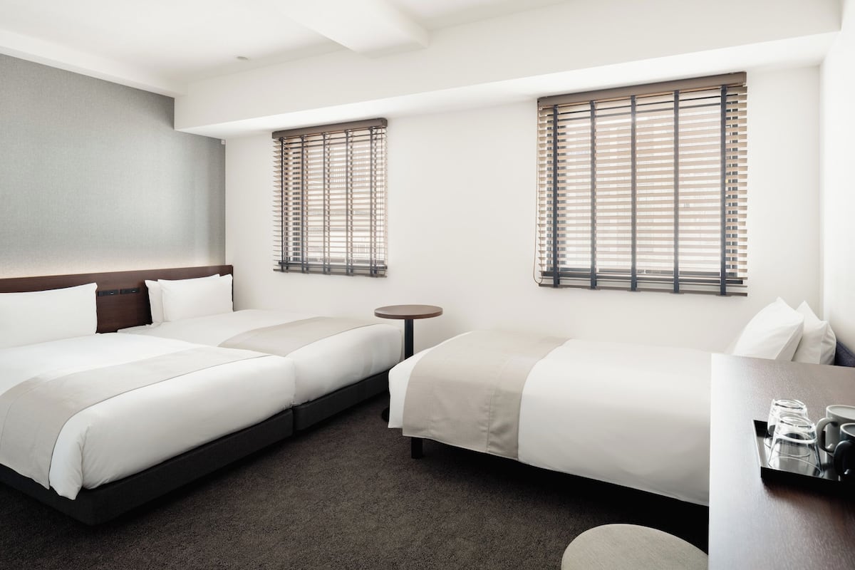 Habitación de hotel con dos camas, una mesita redonda y un escritorio con una bandeja de vasos y una taza.