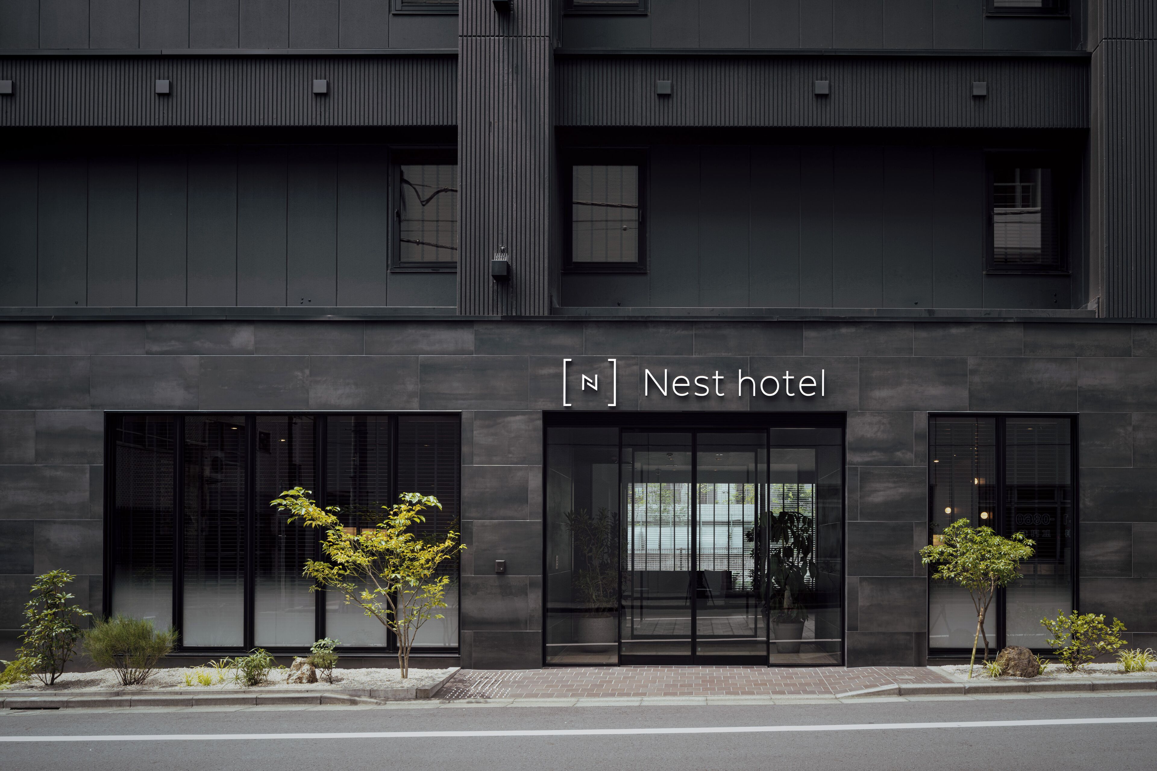 A modern hotel facade with a large entrance, glass doors, and a sign reading "Nest hotel."