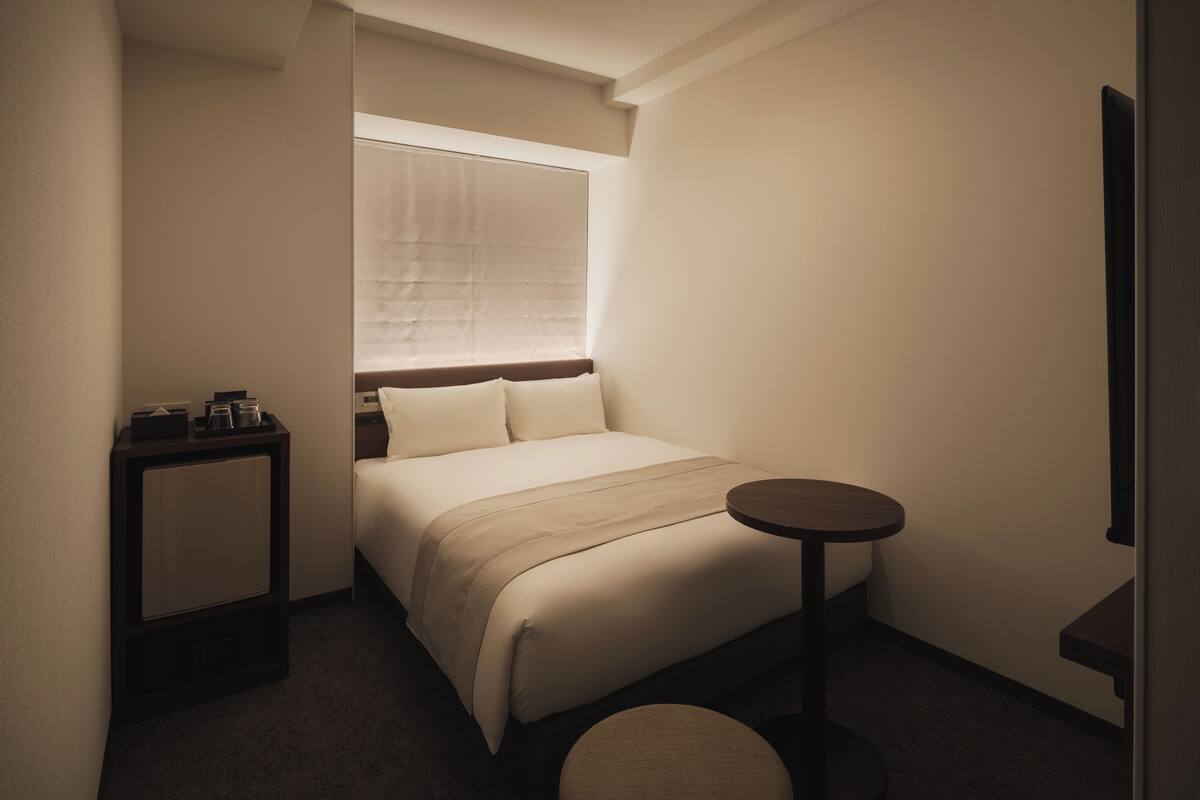 Una habitación de hotel compacta con una cama, una mesita de noche y una pequeña mesa redonda.