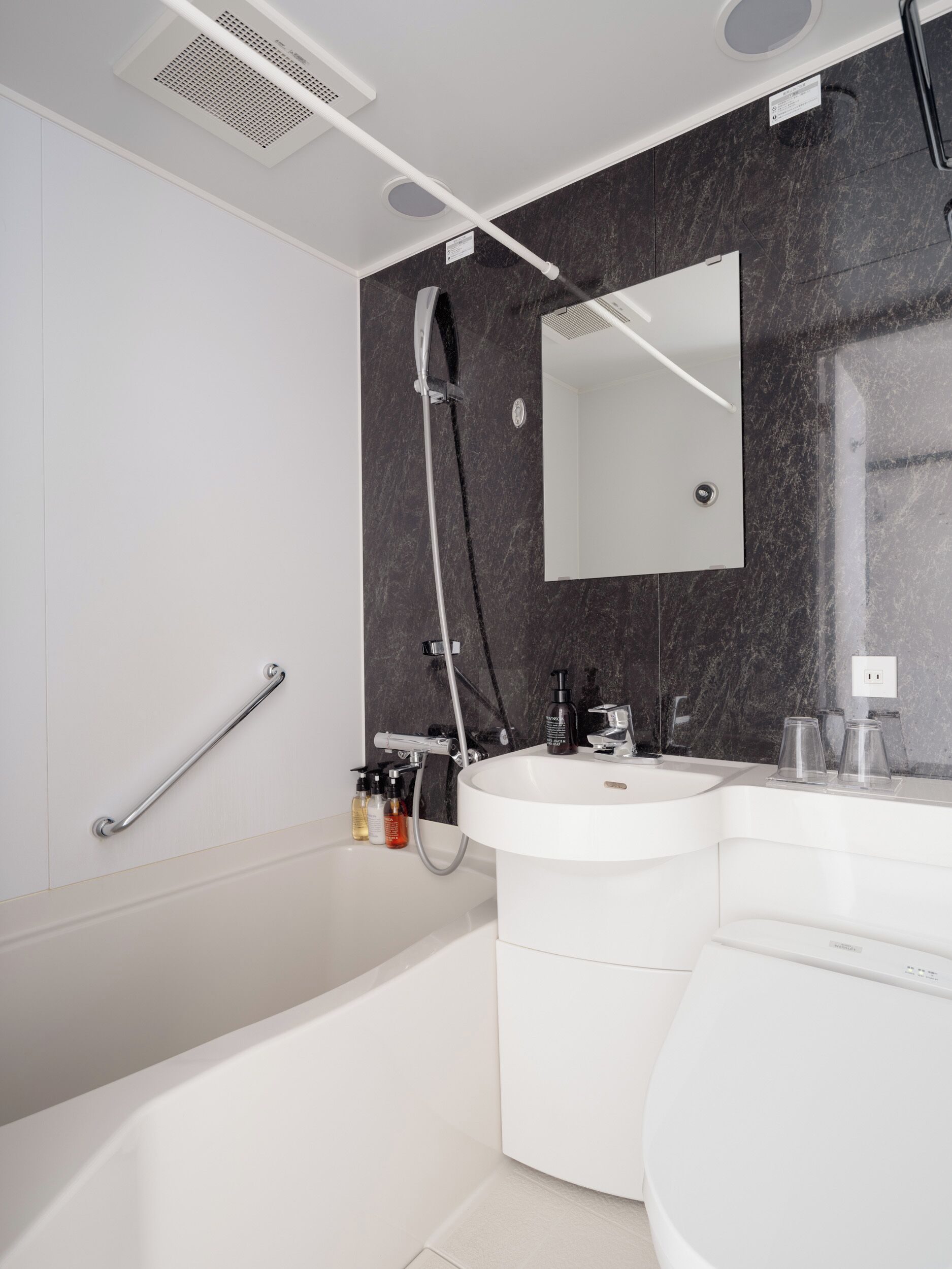 A modern bathroom with a bathtub, a sink, and a shower. There is a handrail on the wall and a mirror above the sink.