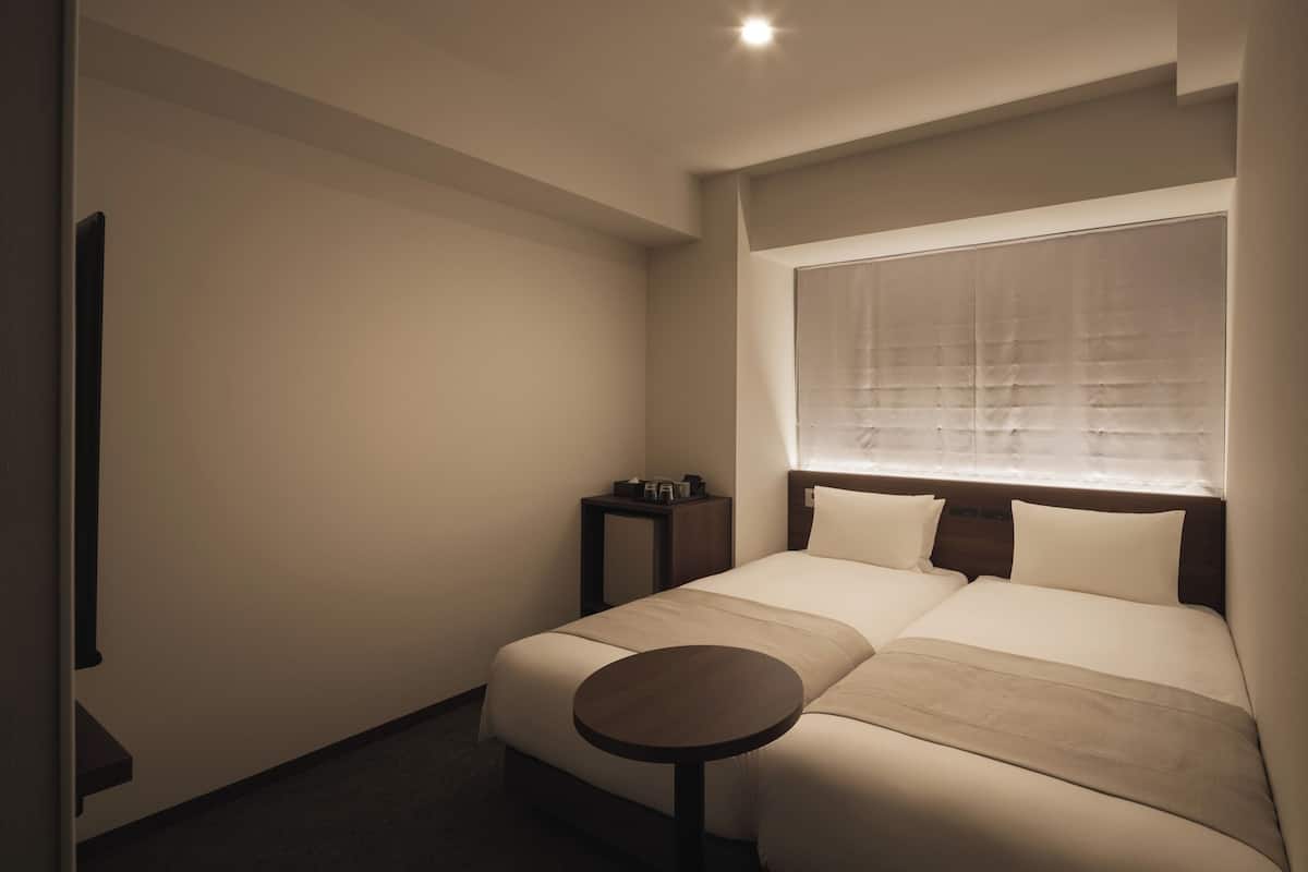Una habitación de hotel con una cama grande, una mesita de noche y una ventana con persianas.