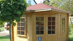 Un petit bâtiment en bois avec un toit rouge, une porte dotée de panneaux de verre et un panneau indiquant un espace de stationnement.