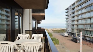 A balcony with white plastic chairs and a table, overlooking a beach and a parking area with a van and a truck. - Apartment Oostduinkerke Near the Beach (Koksijde)