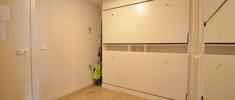 Una habitación con piso de madera, paredes blancas y un armario blanco con varios compartimentos.