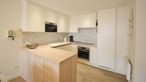 A modern kitchen with wooden cabinets, a central island, a built-in oven, and a stainless steel refrigerator. - Apartment Oostduinkerke Near the Beach (Koksijde)
