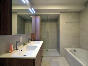 Een moderne badkamer met een wastafelmeubel met dubbele wastafel, een grote spiegel, een inloopdouche en een vrijstaand bad.