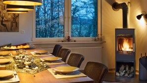 Comedor con una mesa dispuesta para cuatro, chimenea y ventana con vistas a árboles.