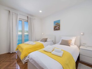 A hotel room with two beds, a balcony with a view, and a painting on the wall.