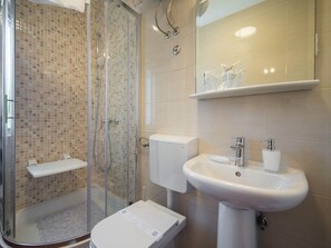 A bathroom with a glass-enclosed shower, a white sink, and a toilet.