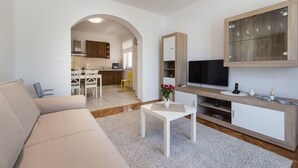 A modern living room with a sofa, a coffee table, and a TV on a wooden cabinet. There is a kitchen visible through an archway. - Apartments Ema-two Bedroom Apartment With Sea View (Ploce)