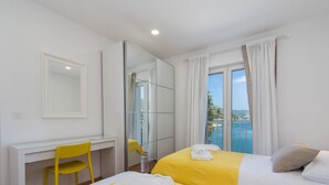 A hotel room with two beds, a desk, a chair, and a large window with a view of the sea. - Apartments Ema-two Bedroom Apartment With Sea View (Ploce)
