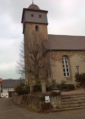 En kirke med et kirketårn, et stort buet vindue og en stenvæg med trapper op til indgangen.