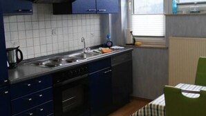 Ett kompakt kök med mörkblå skåp, en diskho i rostfritt stål och ett fönster som släpper in naturligt ljus.